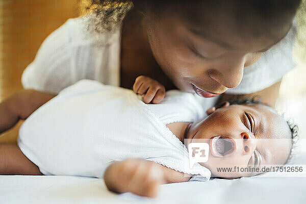 Close-up of mother looking at cute newborn daughter yawning while lying on bed