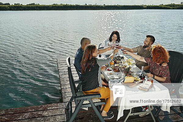 Friends having dinner at a lake clinking wine glasses