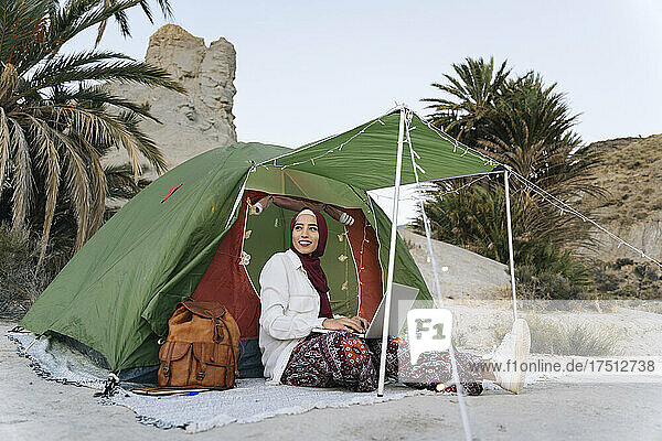 Young woman wearing Hijab using laptop at a tent