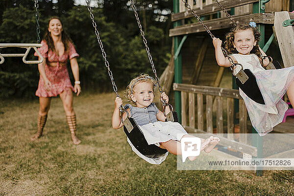 Happy girls on a swing with mother in background