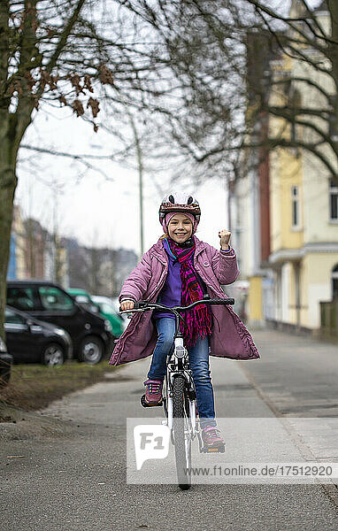 Smiling girl wearing helmet riding bicycle on street in city