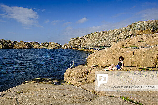 Teenage girl relaxing on rocky shore in summer