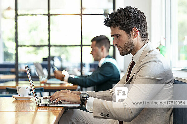 Serious businessman using laptop at table in cafe