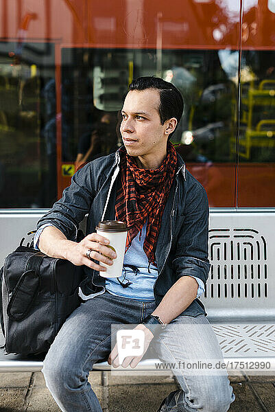 Man in casuals having coffee while waiting for bus at station