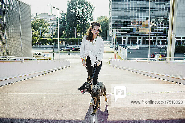 Schöne Frau geht mit Hund auf erhöhtem Gehweg spazieren