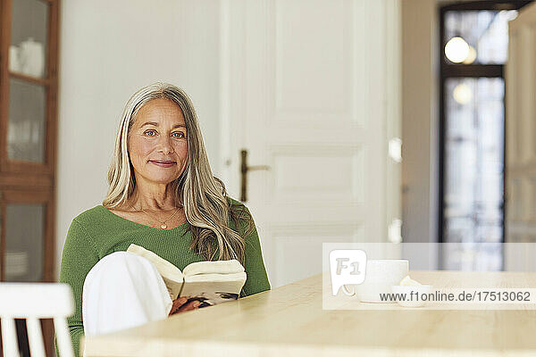Woman with book sitting by table at home