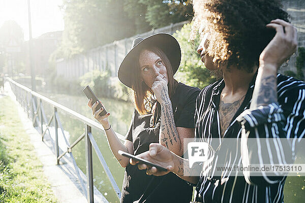Couple holding mobile phones looking at each other while standing in park