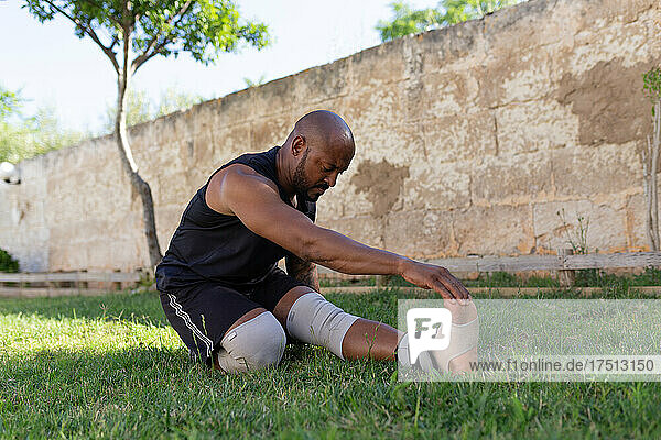 Mature man with shaved head exercising on grassy land against wall in yard