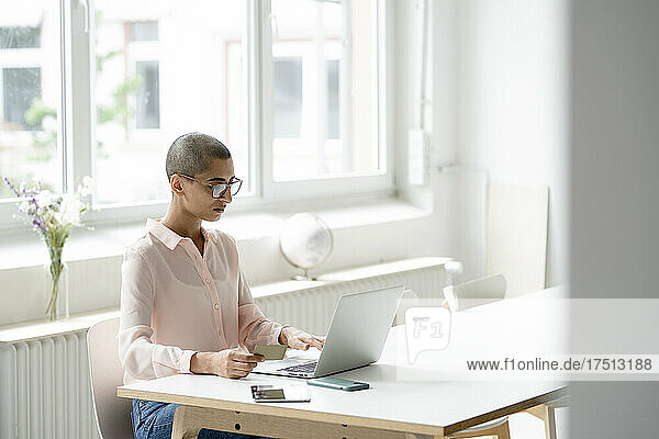 Businesswoman holding credit card and using laptop at desk in loft office