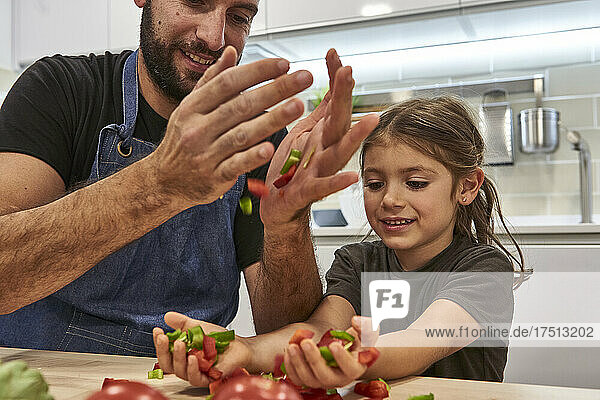 Close-up of father and daughter holding vegetable slices on table in kitchen
