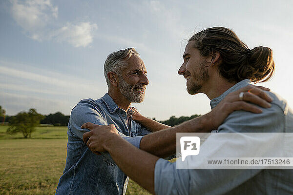 Happy father and adult son facing each other on a meadow in the countryside
