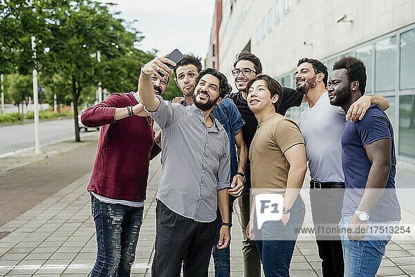 Man taking selfie with male friends while standing on footpath in city