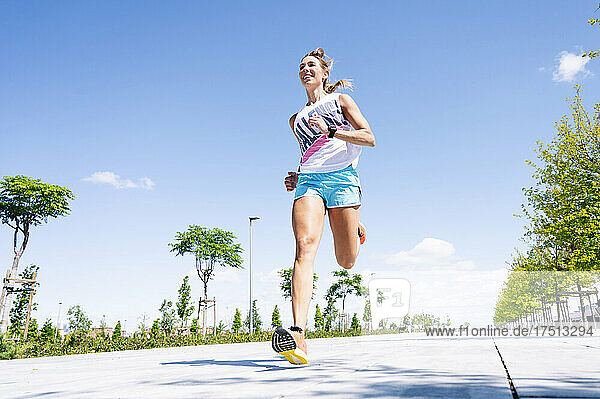 Mid adult woman jogging on street against blue sky