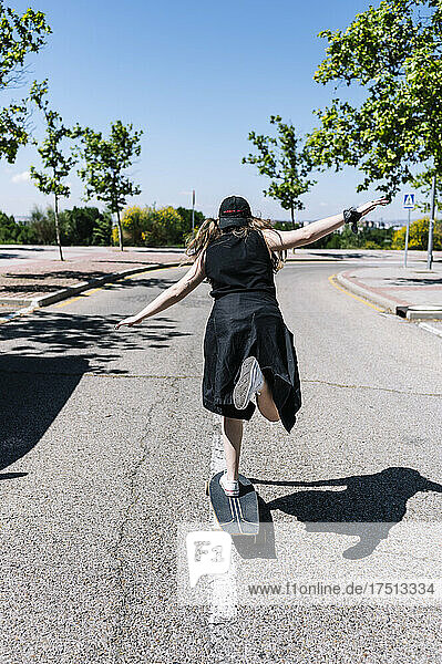 Junge Frau fährt Skateboard entlang der Meridianspitze einer leeren Straße  Rückansicht