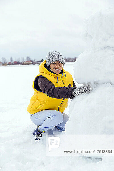 Lächelnde Frau kauert im Schnee und baut einen Schneemann