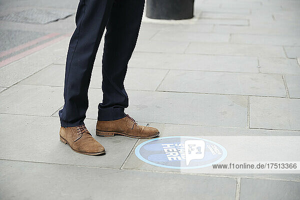 Feet of businessman standing by sign in city