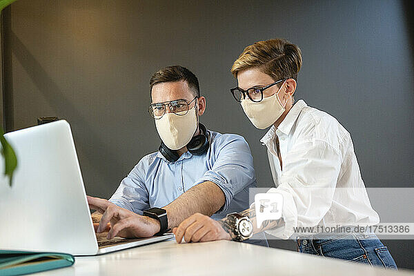 Male and female colleagues planning strategy while discussing over laptop at desk in office during pandemic