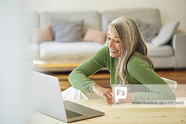 Happy businesswoman looking at laptop while sitting by table