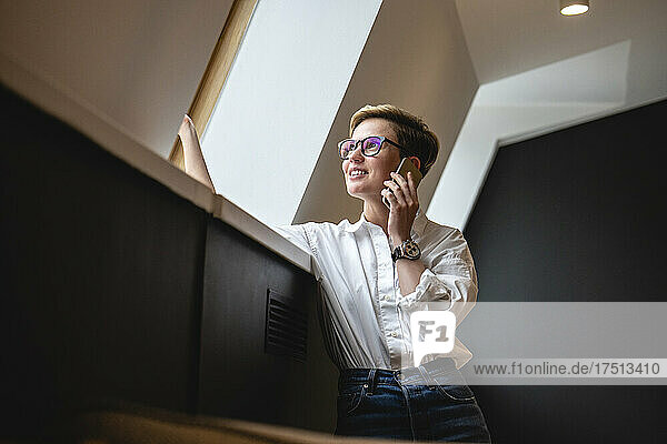 Smiling businesswoman talking on smart phone while looking through window in office cafeteria