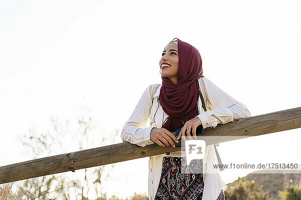 Smiling young tourist woman wearing Hijab leaning on wooden railing