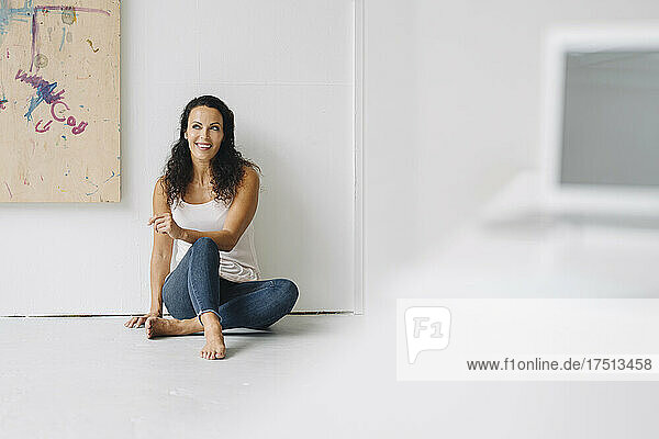 Thoughtful woman looking away while sitting on floor against wall in loft