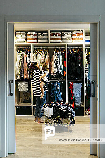 Mother with daughter choosing clothes in dressing room at home seen through doorway