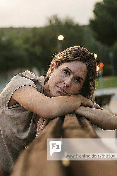 Close-up of thoughtful mid adult woman leaning on railing in park at sunset