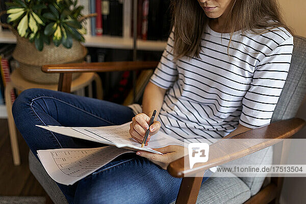 Nahaufnahme einer Geschäftsfrau  die ein Dokument liest  während sie im Heimbüro auf einem Stuhl sitzt