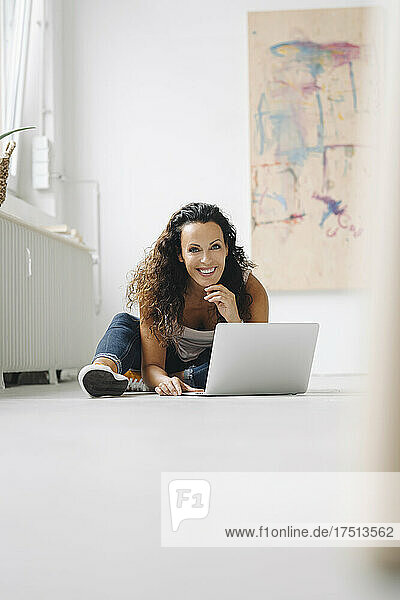Lächelnde Frau mittleren Alters  die zu Hause einen Laptop auf dem Boden benutzt