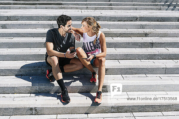 Smiling couple looking at each other while sitting on steps in city during sunny day
