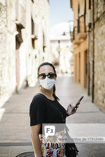 Woman wearing protective ask and using smartphone in alley