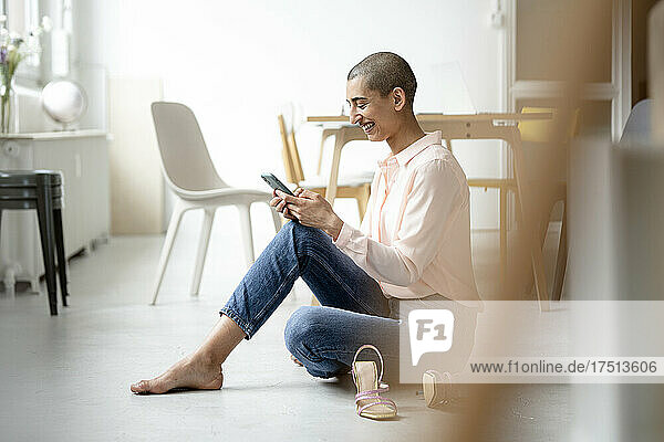 Happy woman sitting on the floor in a loft using smartphone