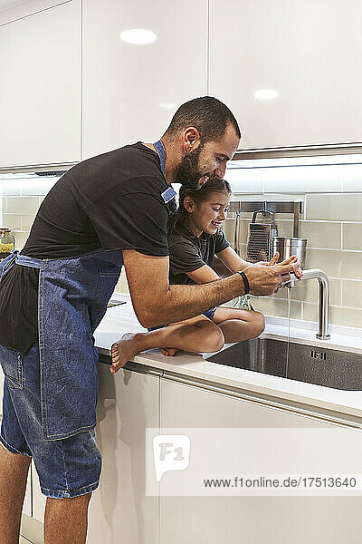 Father and daughter washing hands in kitchen sink at home
