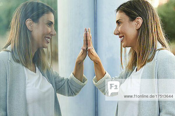 Symmetrical image of smiling businesswoman touching window glass