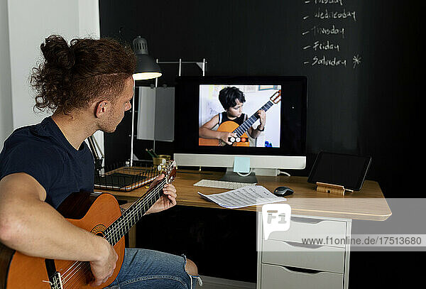 Man learning guitar while watching tutorial at home
