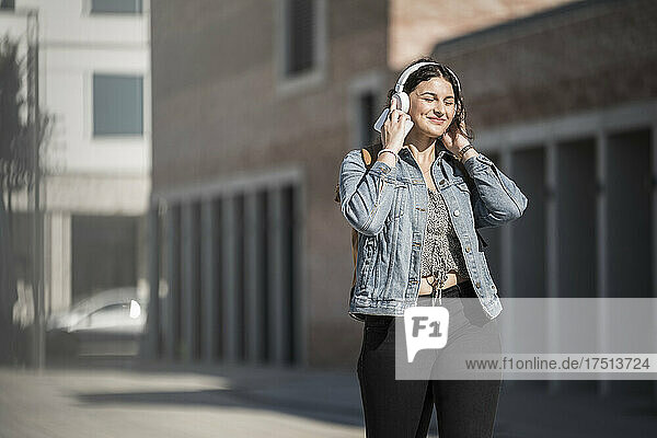 Smiling female commuter listening music through headphones while walking on street in city