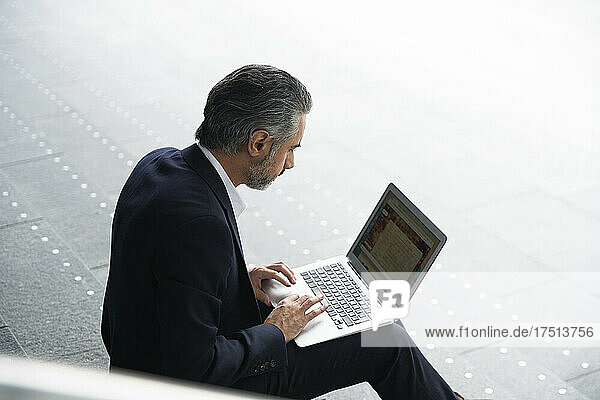 Businessman using laptop on steps in city