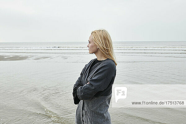Niederlande  blonde junge Frau steht am Strand und blickt in die Ferne
