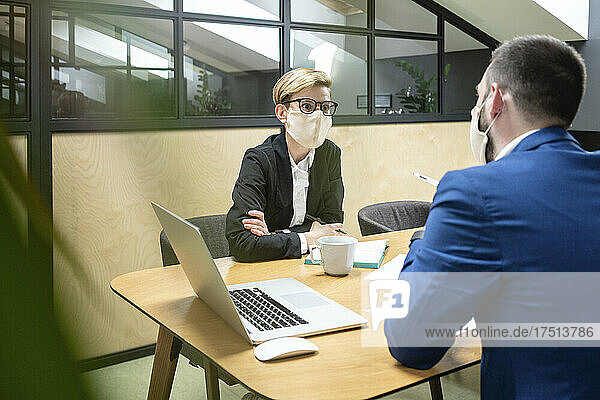 Female and male colleagues wearing masks while planning strategy at desk in board room during epidemic