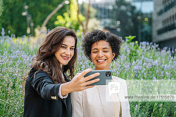 Positive young diverse women taking selfie on smartphone in city park