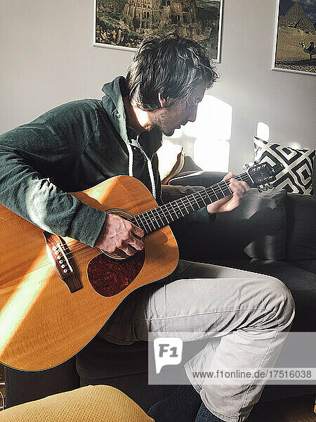 Young man sitting on the couch and playing guitar