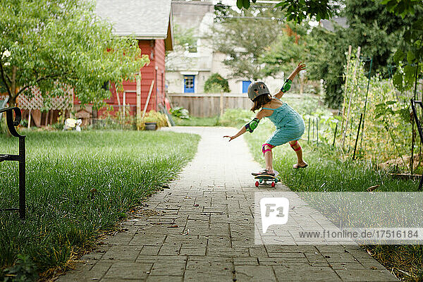 A small child balances one foot on skateboard on backyard path