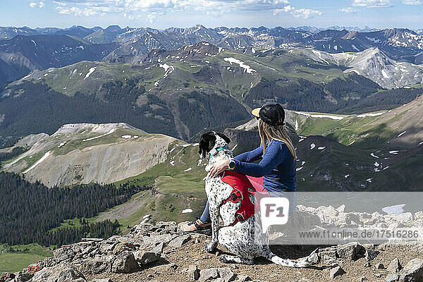 Female hiker sitting on mountain with dog during sunny day