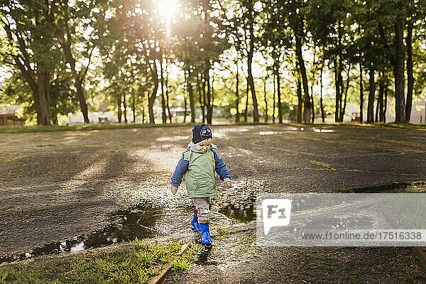 Toddler boy walking in wellies and green and blue jacket in park