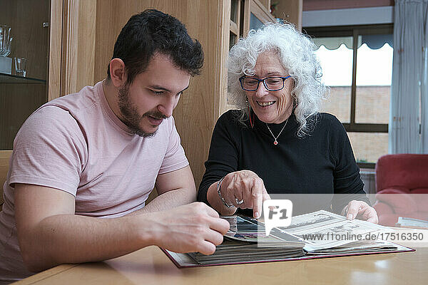 Mature mother and adult son spend time together and look at old album.