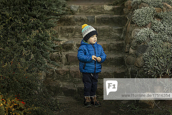 Standing boy in blue jacket in front of stone stairs in garden