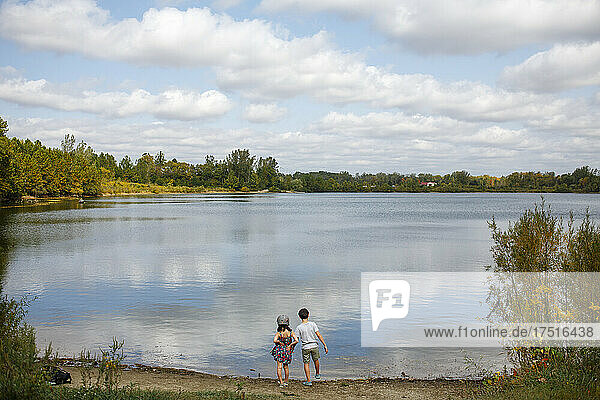 Two small children stand by lake on sunny summer day