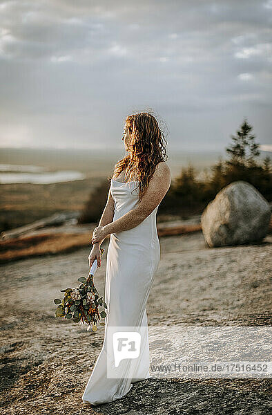 red haired bride with flowers looking out at view from mountain