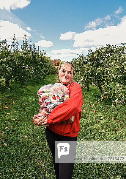 Happy teen girl holding bag of fresh picked apples in an orchard.