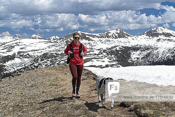 Smiling woman hiking with dog against snow covered mountain